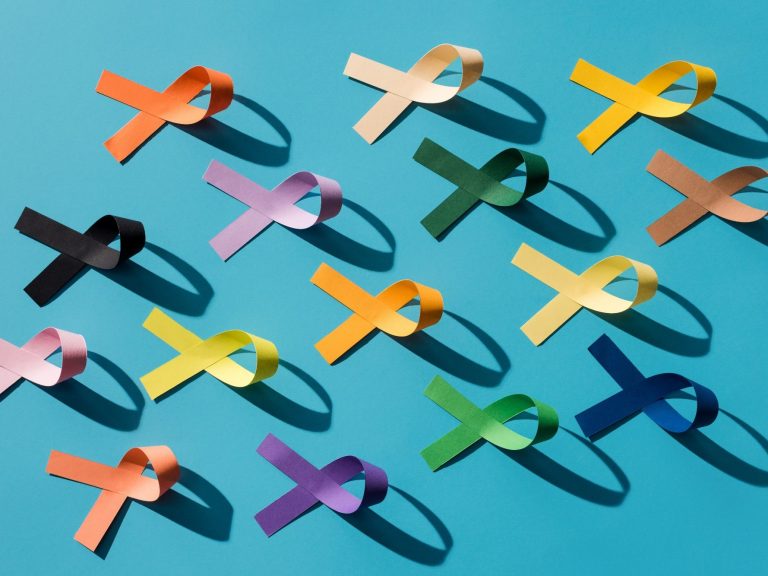Colorful awareness ribbons arranged on a teal background, casting soft shadows.