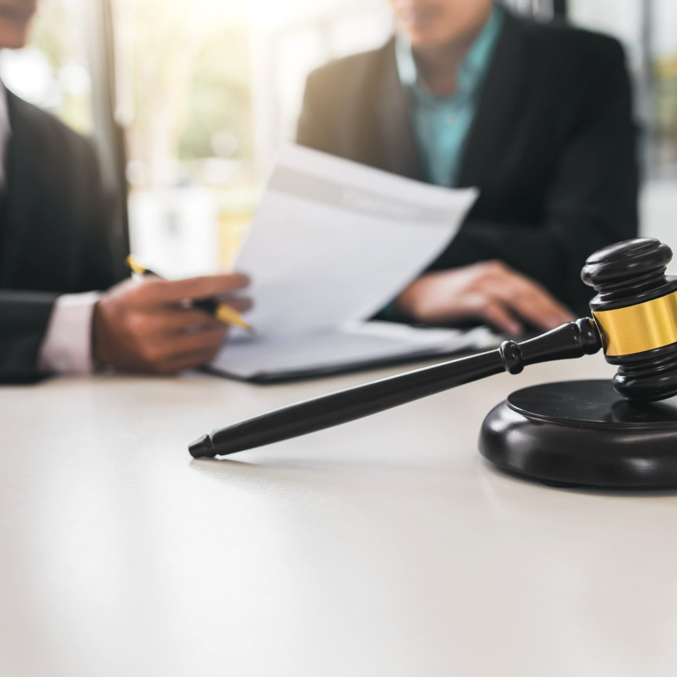 A gavel on a table near people reviewing legal documents.