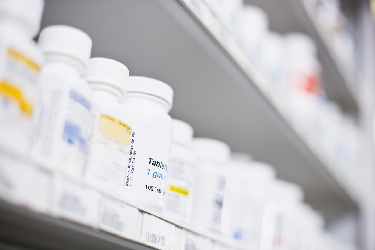 Rows of white prescription medicine bottles on a pharmacy shelf.