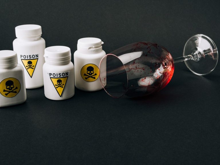 White bottles with poison symbols beside a tipped wine glass on a dark background.