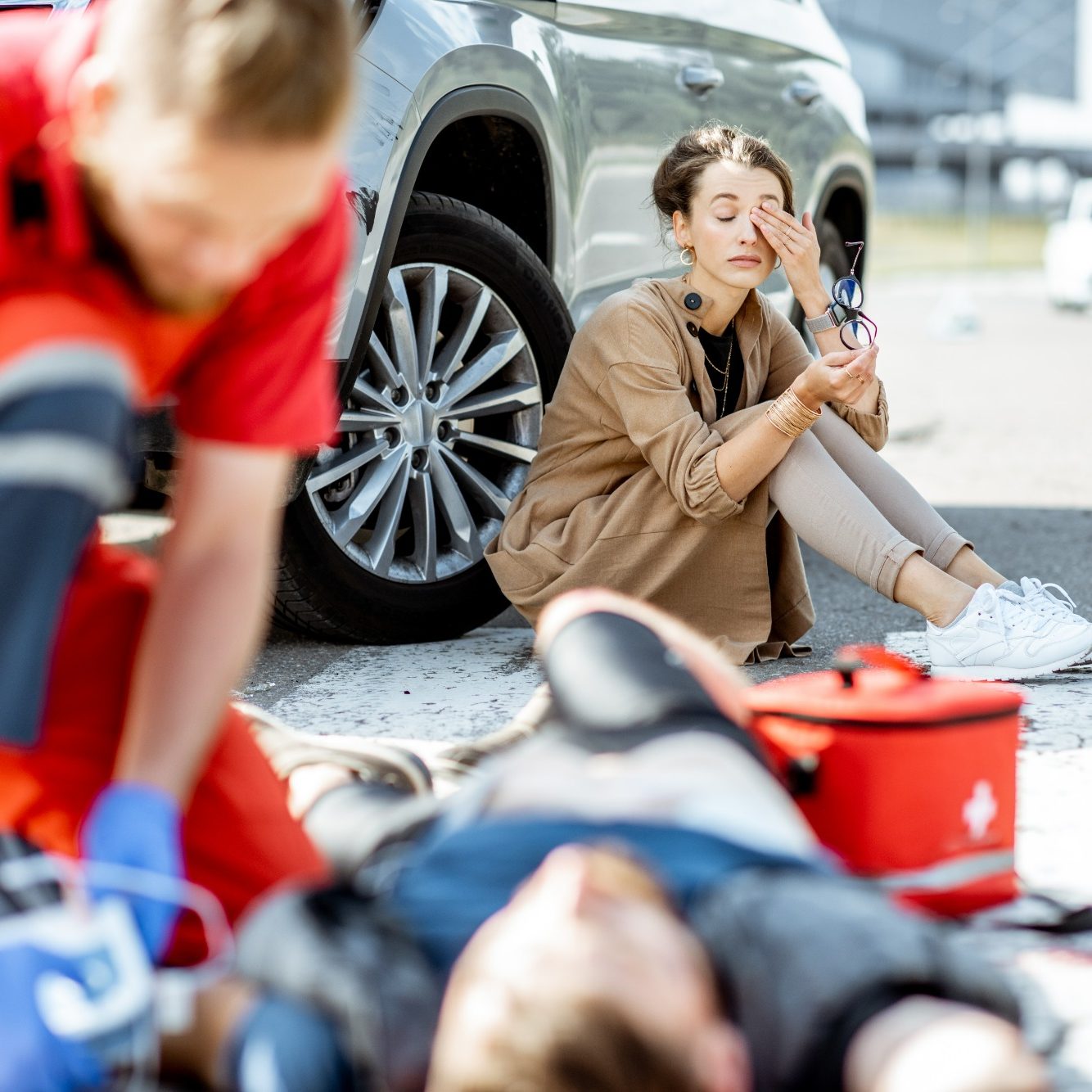 Emergency responders attend to an injured person while a bystander looks on anxiously.